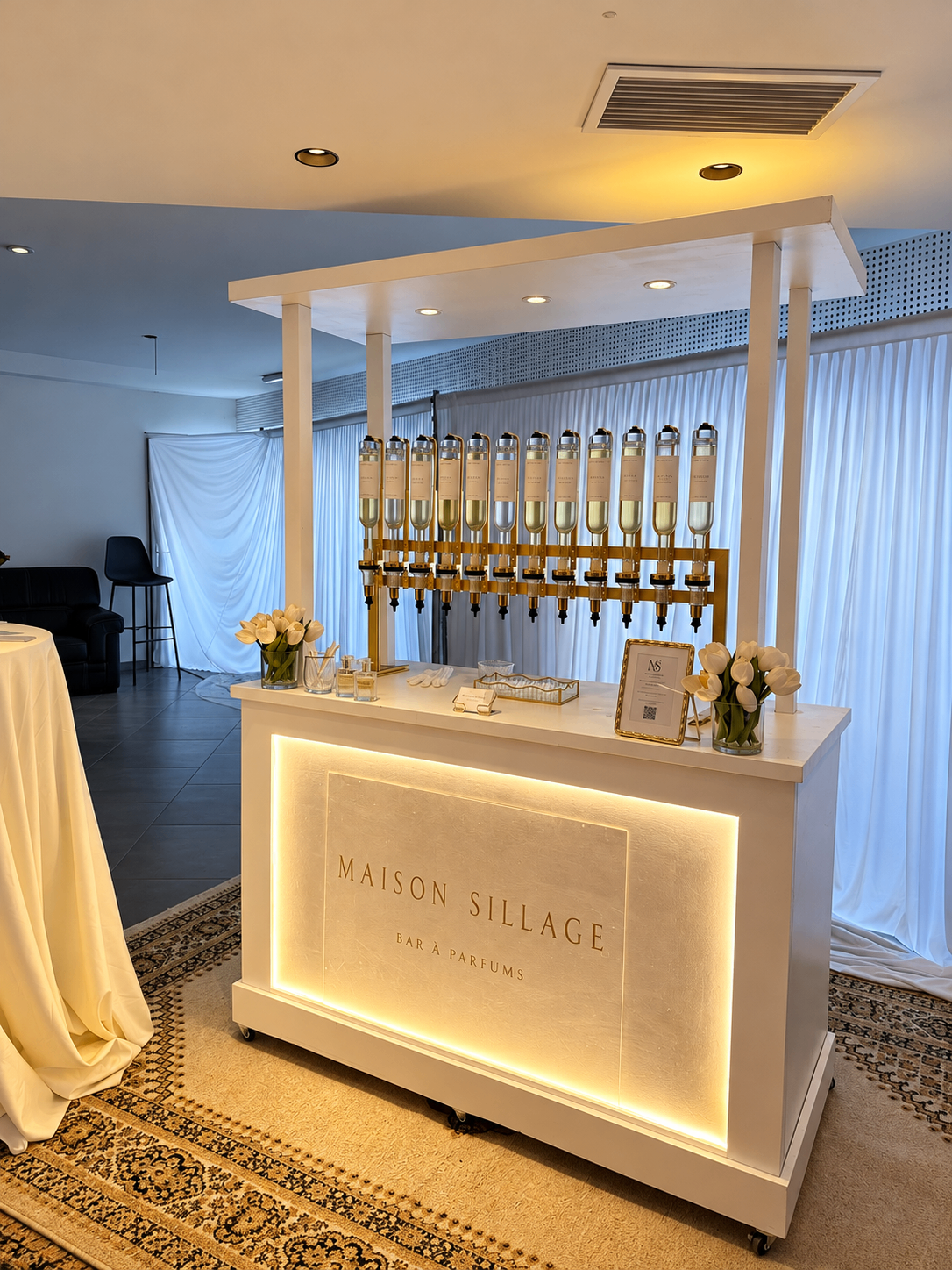 Bar à parfum installé dans une salle de réception habillée de voilages blancs