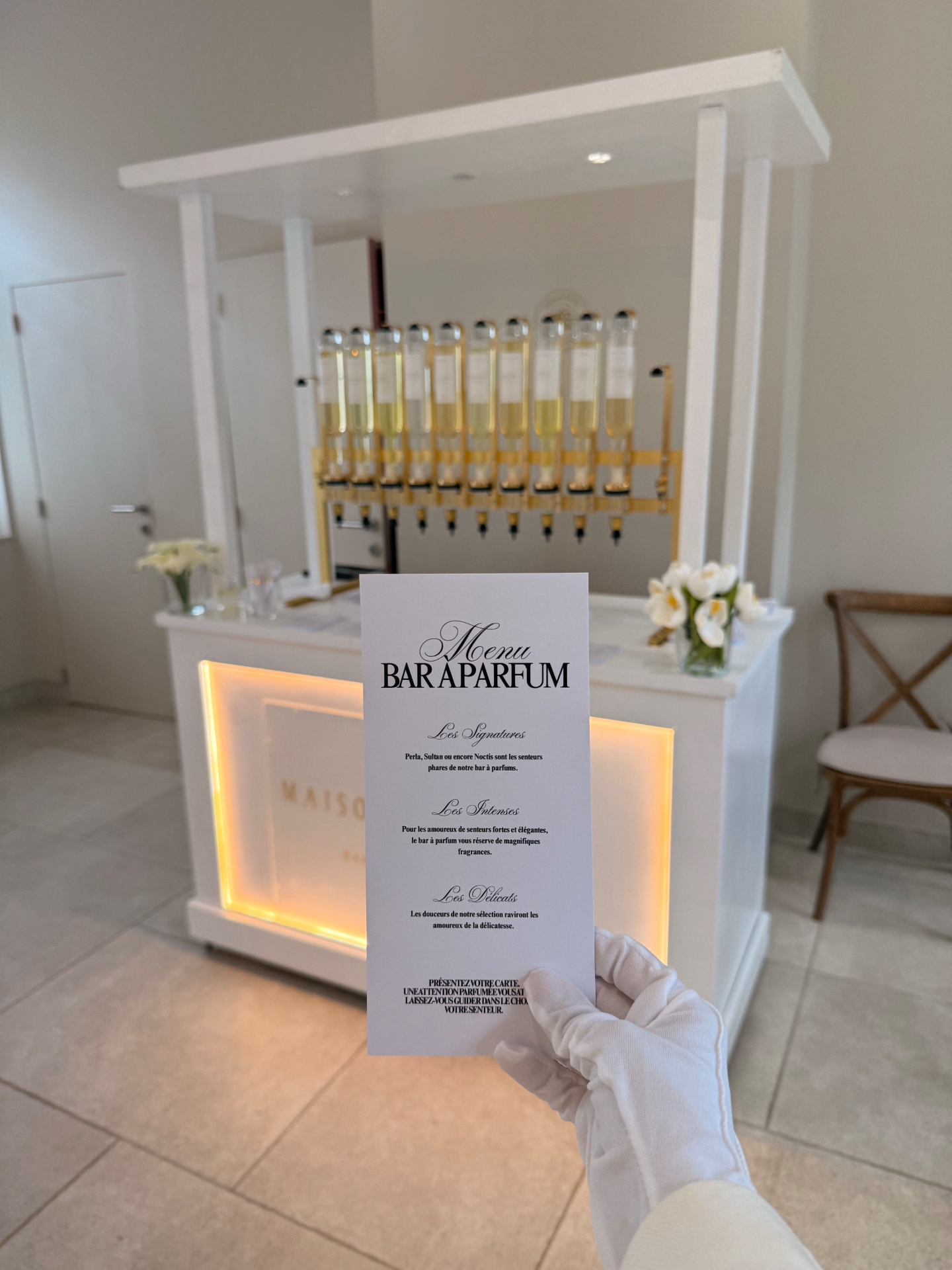 Menu du bar à parfum tenu d’une main gantée de blanc, le comptoir en arrière-plan