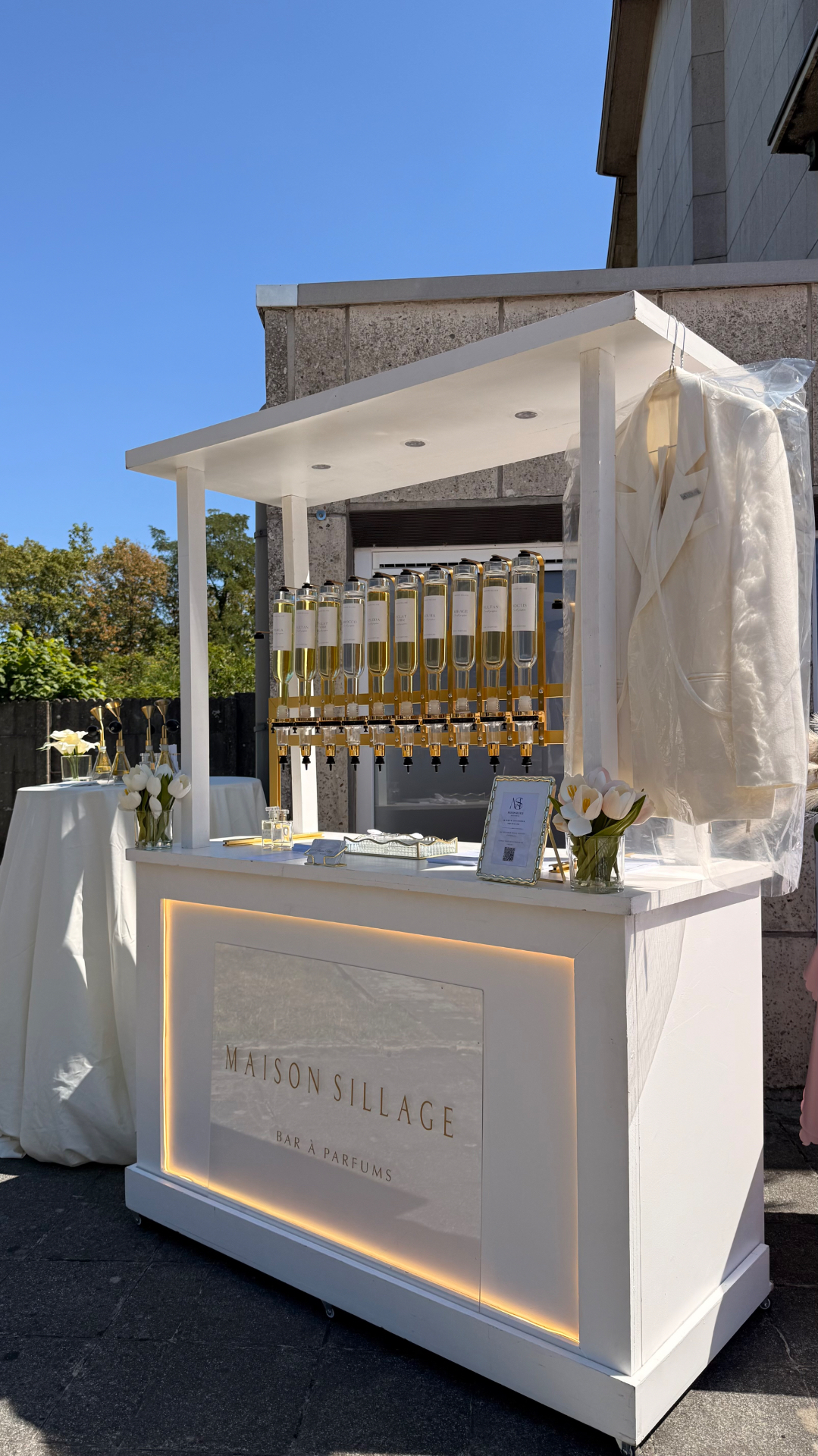 Bar à parfum installé en extérieur sous un ciel bleu, tulipes blanches sur le comptoir